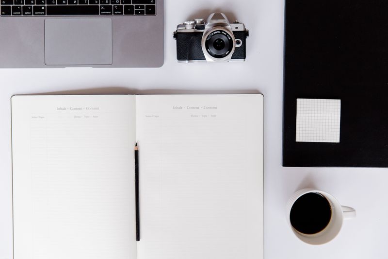 An open notebook, laptop, camera, and coffee on a planning desk